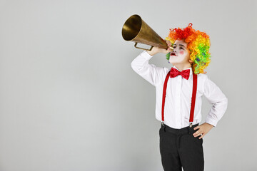 Little boy dressed like clown with megaphone on grey background, space for text. Surprise party