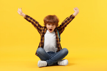 Cute schoolboy with backpack and book on orange background