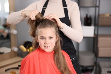Naklejka premium Hairdresser doing girl's hairstyle in salon, closeup