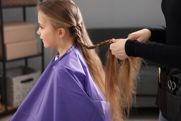 Fototapeta premium Hairstylist braiding girl's hair in salon, closeup
