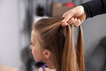 Hairstylist braiding girl's hair in salon, closeup