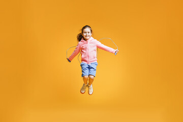 Cute little girl with jump rope on yellow background