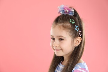 Happy little girl wearing beautiful hair accessories on pink background, space for text