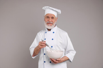 Professional pastry chef with bowl and whisk on grey background