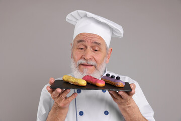 Professional pastry chef with delicious eclairs on grey background
