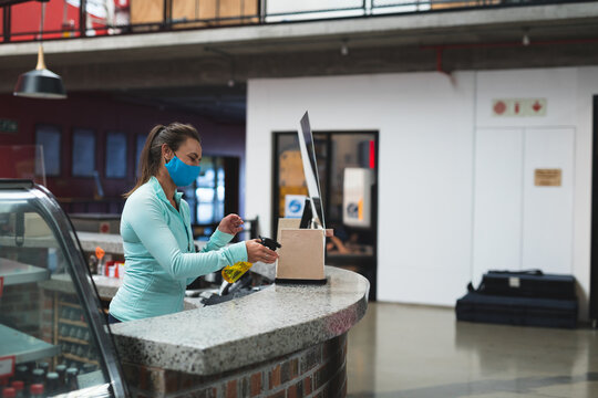 Mid-adult woman spraying disinfectant with yellow spray bottle onto box behind reception counter