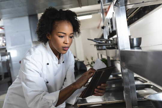 Young adult African American chef reviewing order ticket and tablet at commercial kitchen counter - Powered by Adobe