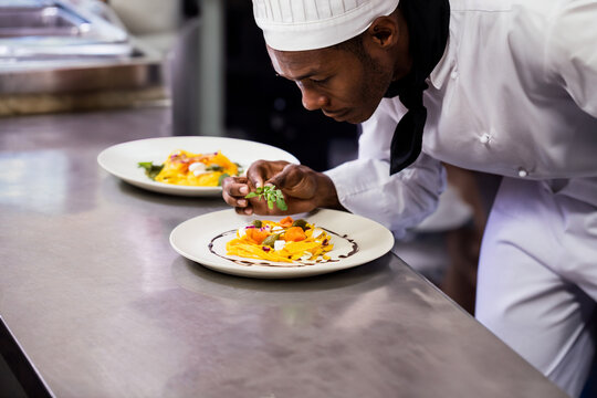African American male chef plating microgreens on plate in restaurant kitchen, copy space