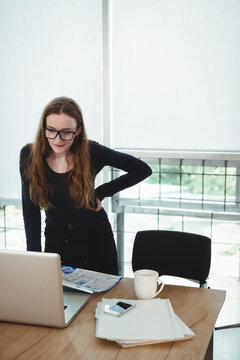 Young adult woman leaning over laptop at office, with documents and coffee mug, copy space