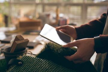 Person's hands holding tablet and turf swatch at indoor workshop, including wooden blocks
