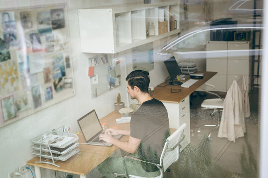 Man typing on laptop at desk in modern office, with potted plant and bulletin board