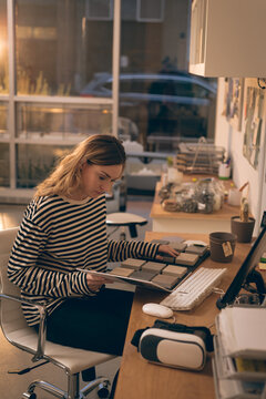Female designer holding sample swatch book and examining samples in design studio, with VR headset