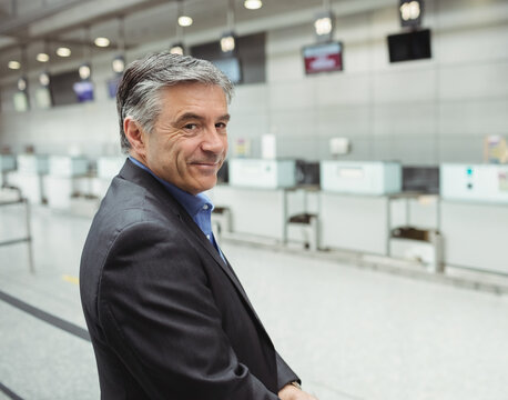 Middle aged man standing at airport check-in counters, with digital monitors, barrier, copy space