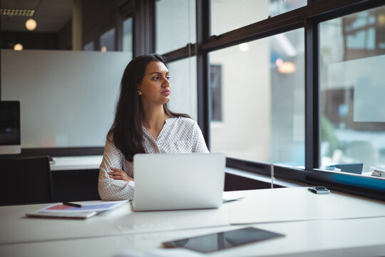 Woman sitting at desk in modern office, using silver laptop with smartphone, notebook and papers