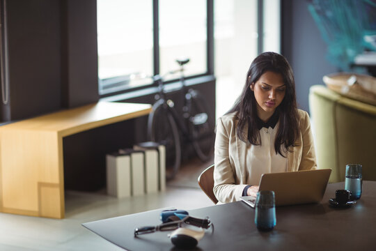 Businesswoman working on laptop at modern coworking table by windows, with VR headset and bicycle