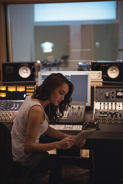 Asian woman working at mixing console in recording studio control room, reviewing tablet