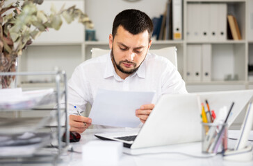Obraz premium European male office worker sitting at desk and doing paperwork.