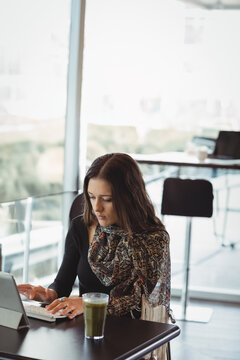 Woman typing on tablet with detachable keyboard at caf&eacute; table, sipping green smoothie