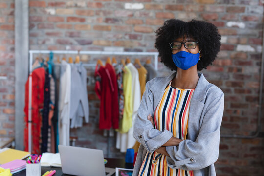 Woman standing by clothing rack in fashion studio wearing face mask and eyeglasses, copy space