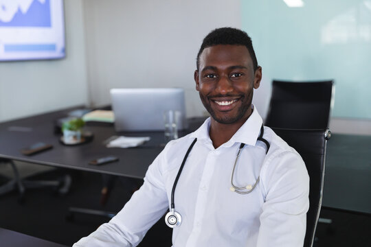 Young African American doctor sitting at table in office, smiling with stethoscope and laptop - Powered by Adobe
