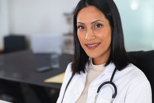 Female doctor sitting in clinic, with stethoscope, glass of water, smartphone, folder, copy space