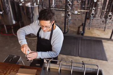 Mid-adult man twisting aluminum can lid on wooden counter in brewery, with tanks and machinery
