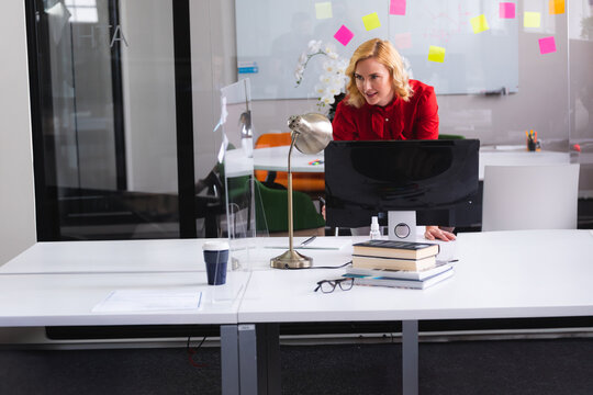 Businesswoman leaning over desk in office, with computer monitor, coffee cup, copy space