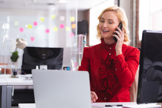 Woman handling smartphone and typing on laptop in open?plan office, with sticky notes, copy space