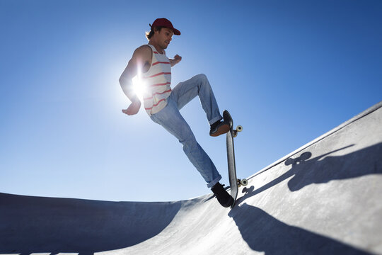 Male skateboarder performing trick on concrete bowl ramp at skate park, capturing sun flare effect