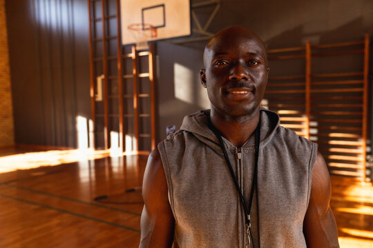 African American mature adult male coaching basketball in school gym, with whistle on hoodie