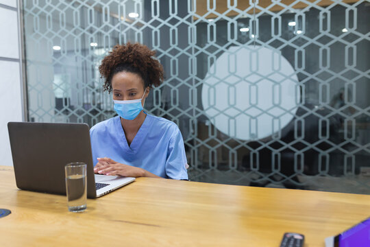 Woman typing on laptop in meeting room with water glass, remote control, purple folder, copy space
