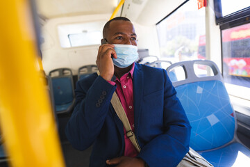 Mature African American man riding city bus talking on phone with messenger bag while wearing mask