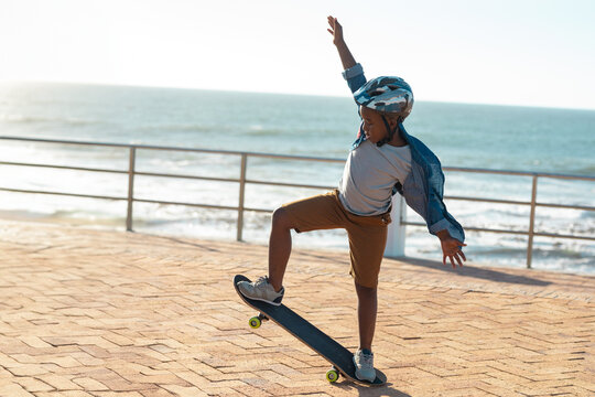 African American child boy balancing on skateboard at seaside promenade, wearing helmet, copy space