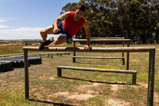 Man jumping over wooden hurdle on rural obstacle course, with stacked tractor tire obstacles