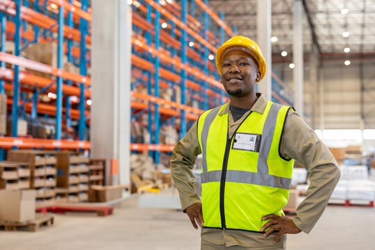 African American man checking stock in warehouse wearing yellow hard hat, with ID badge, copy space