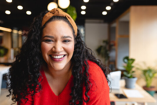 Professional woman leaning forward toward camera in coworking office, with laptop and plants