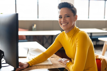 Woman smiling while using computer in co?working space, with monitor and smartphone, copy space