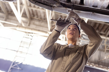 Female mechanic working beneath vehicle undercarriage in garage, using ratchet wrench and gloves
