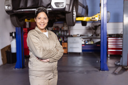 woman mechanic standing in automotive repair shop, with hydraulic lift, tool cabinets and workbench - Powered by Adobe