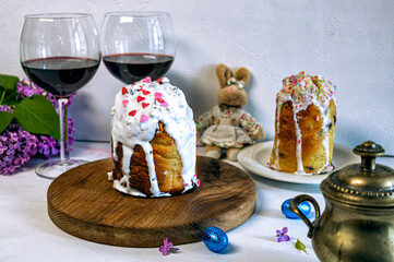 Easter cake or sweet bread decorated with white icing, red coloured Paschal eggs, spring flowers, white wooden table and window background. Easter treat, holiday decorations, symbols:  bunny.