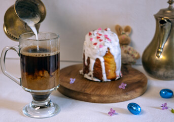 Easter cake or sweet bread decorated with white icing, red coloured Paschal eggs, spring flowers, white wooden table and window background. Easter treat, holiday decorations, symbols:  bunny.