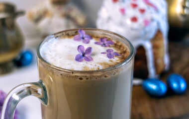 Easter cake covered with icing with a decor of a chocolate nest with eggs and a chicken topper on a white plate on a marble background. Easter table, treats, decor, traditions concept. Modern style, 