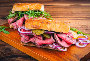 Traditional sliced cold cuts roast beef sandwich with onion, gherkin and onion as close-up on a wooden board