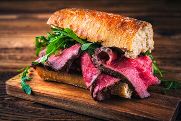Traditional sliced cold cuts roast beef sandwich with rucola served as close-up on a wooden design cutting board