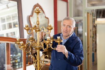 Mature man restorer with brush removes dirt and dust deposits from multi-level bedside antique candelabra for 9 lamp