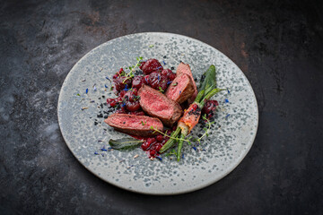 Traditionally roasted fillet of saddle of venison with chestnuts, bacon-wrapped bean sticks and redcurrants served with lingonberry sauce as close-up in a bowl with a rustic background