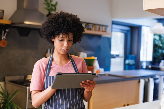 Young woman using digital tablet while cooking in modern home kitchen, wearing striped apron