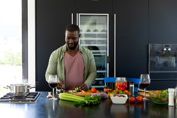 Young African American man slicing vegetables in modern kitchen, with chef's knife on cutting board