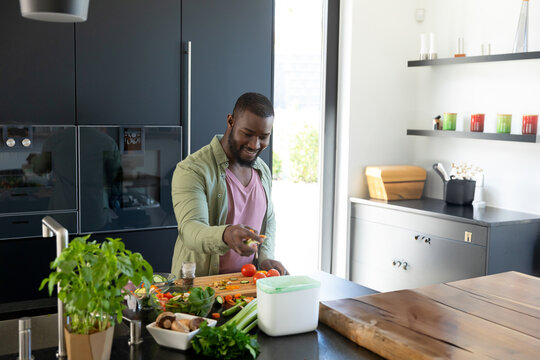 Young African American man chopping vegetables on kitchen island, with cutting board and knife