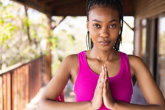 Young adult African American woman holding prayer pose on wooden veranda, surrounded by greenery
